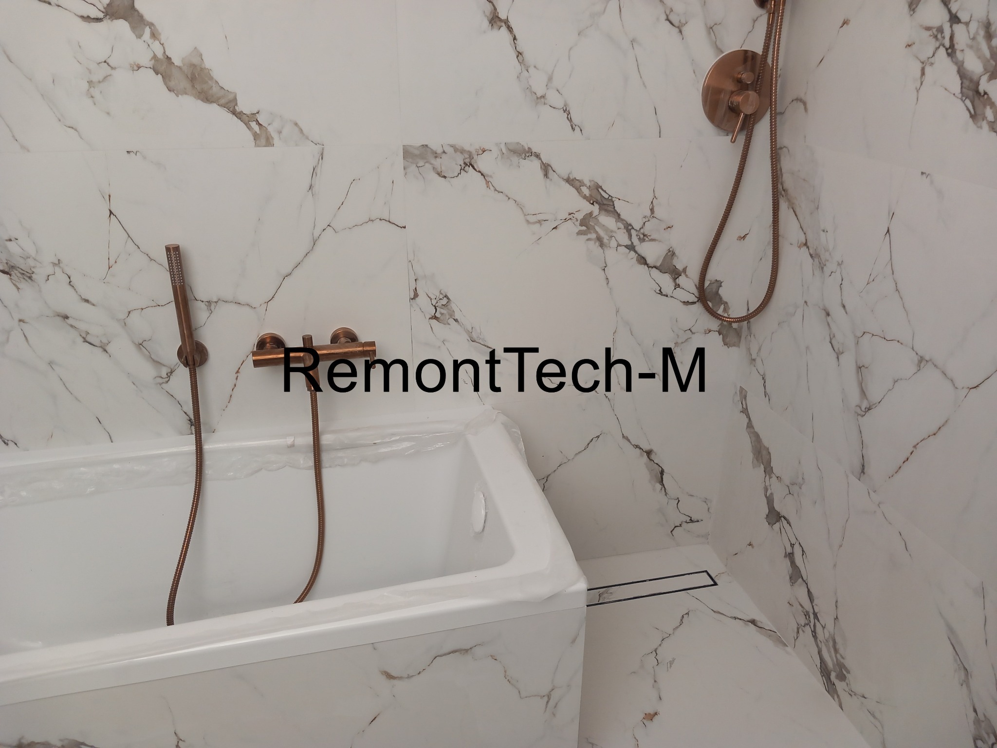 Wykończona łazienka z wanną, marmurowe płytki na ścianach i podłodze, armatura w odcieniach miedzi. Widoczny odpływ liniowy.