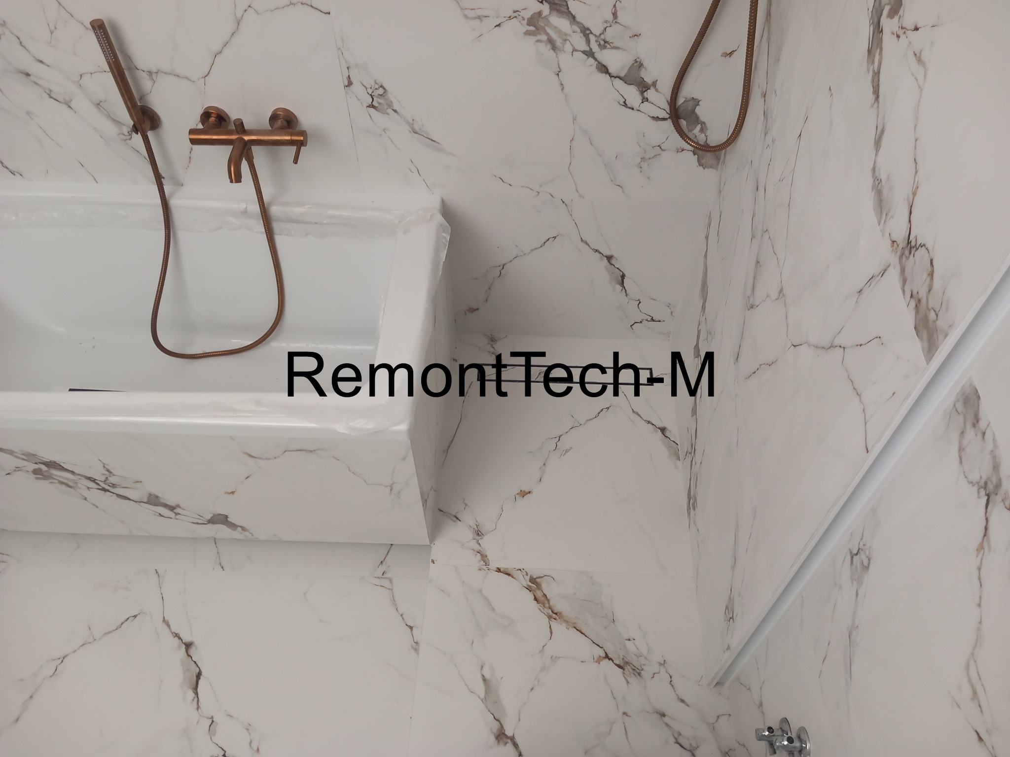 Wykończona łazienka z wanną i armaturą w odcieniach brązu. Płytki imitujące marmur na ścianach i podłodze. Nowoczesny design z dbałością o detale.