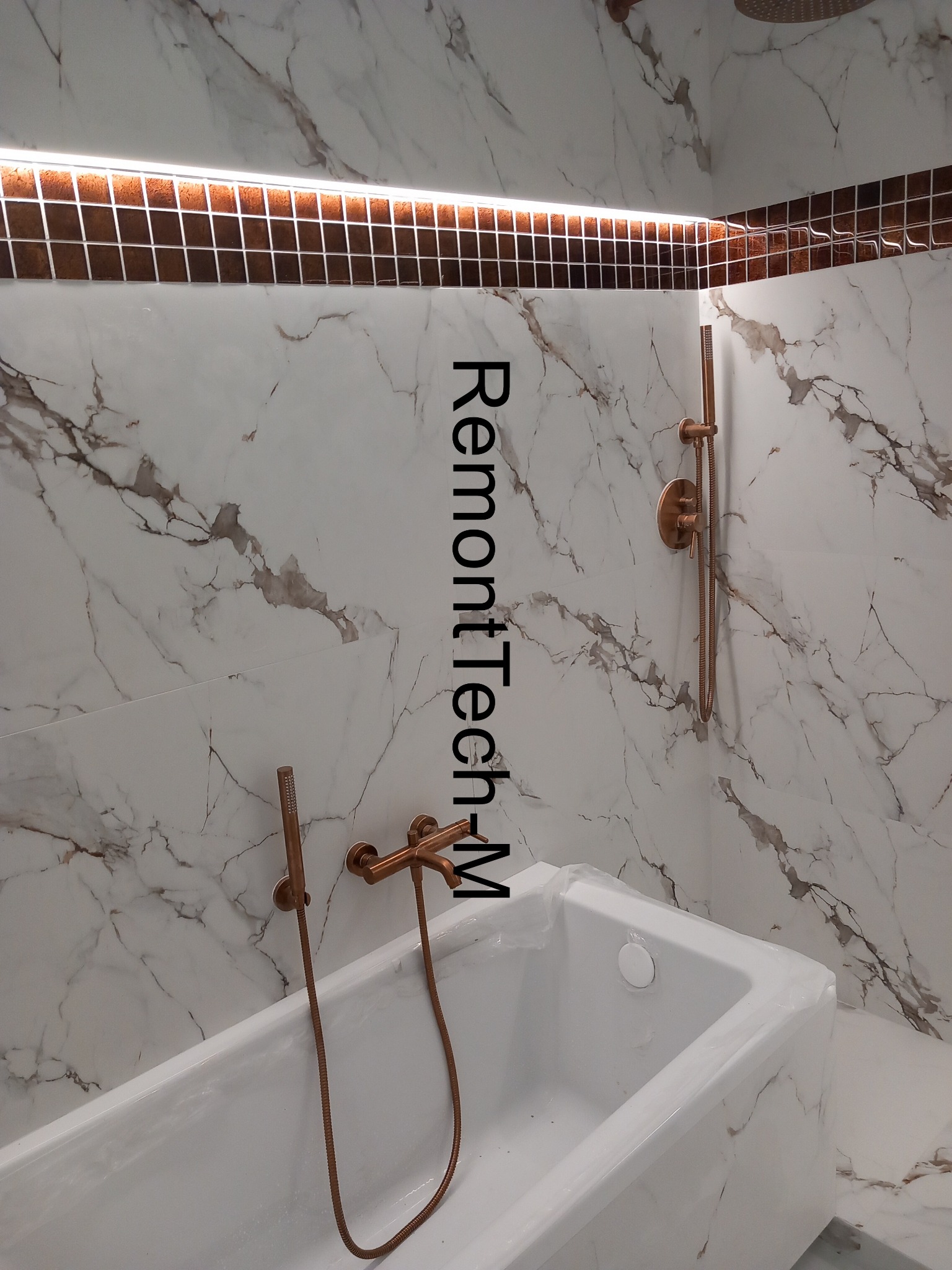 Wykończona łazienka z wanną obudowaną marmurowymi płytkami i brązową armaturą. Nad wanną widoczna listwa z oświetleniem LED.