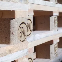 Stos drewnianych palet euro z widocznymi znakami EPAL, ułożonych w magazynie w jasnym świetle.