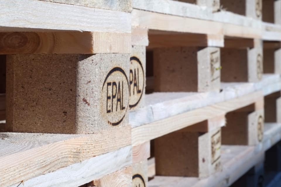 Stos drewnianych palet euro z widocznymi znakami EPAL, ułożonych w magazynie w jasnym świetle.