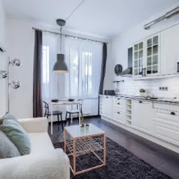 Nowoczesne wnętrze: biała kuchnia z czarnymi akcentami, stół z krzesłami, sofa z poduszkami i dywanem w salonie.