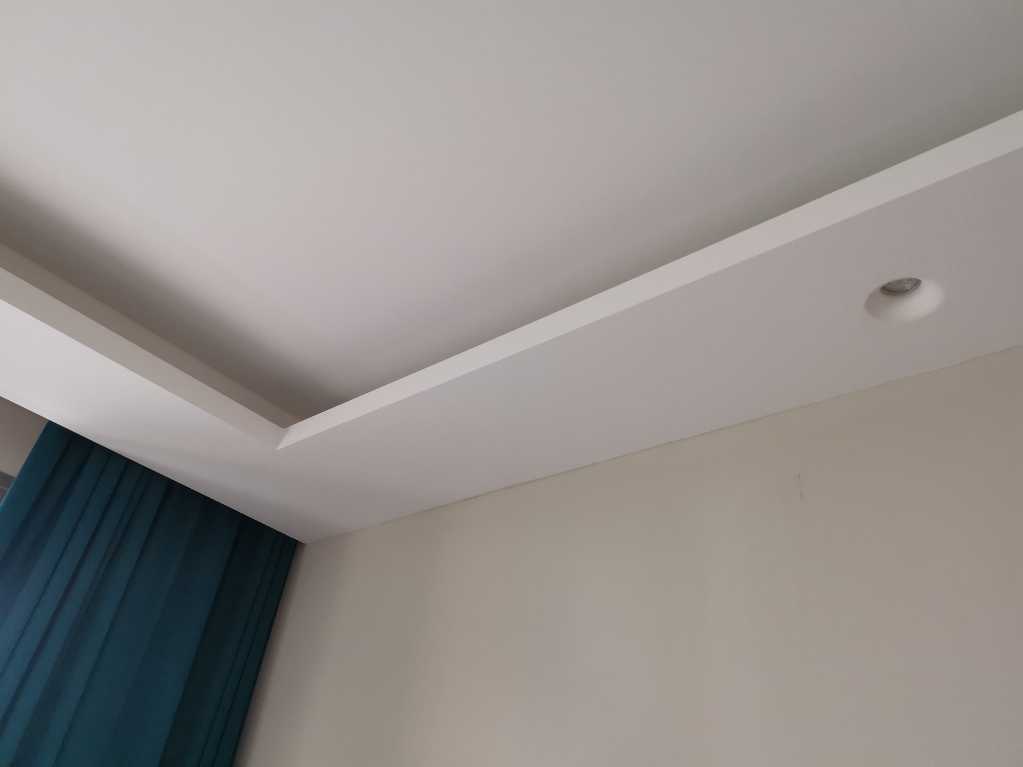 Wykończony sufit z płyt kartonowo-gipsowych z wbudowanym oświetleniem punktowym i fragmentem zasłony w kolorze butelkowej zieleni.