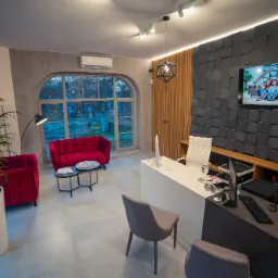 Nowoczesne biuro nieruchomości z czerwonymi sofami, dużym oknem i ścianą z telewizorem wyświetlającym rodzinę.