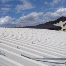 Montaż konstrukcji wsporczej pod panele słoneczne na blaszanym dachu budynku mieszkalnego, widoczne uchwyty i szyny montażowe przed instalacją paneli.