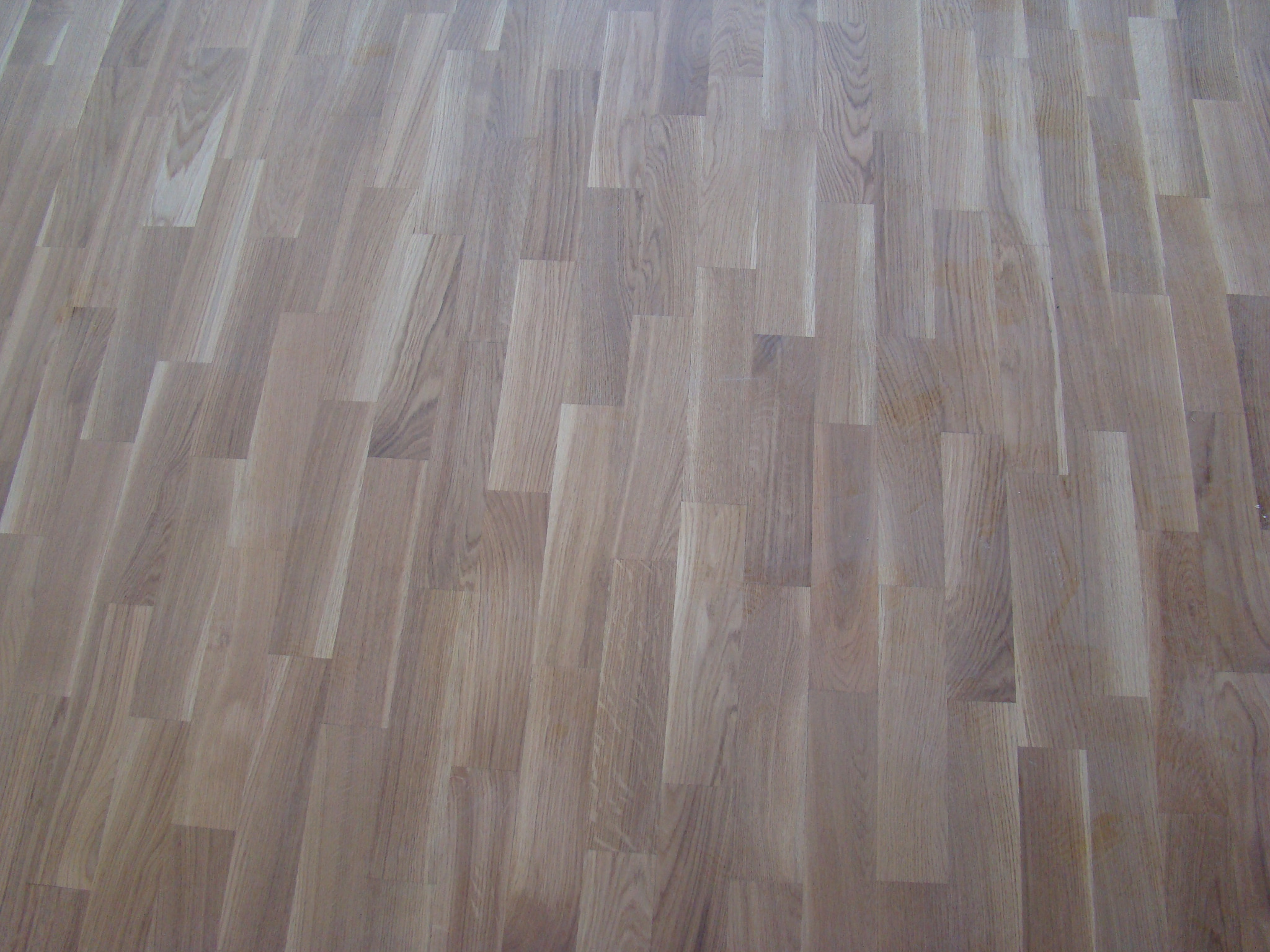 Jasny, dębowy parkiet ułożony w regularny wzór, z widocznymi słojami drewna i delikatnym połyskiem.