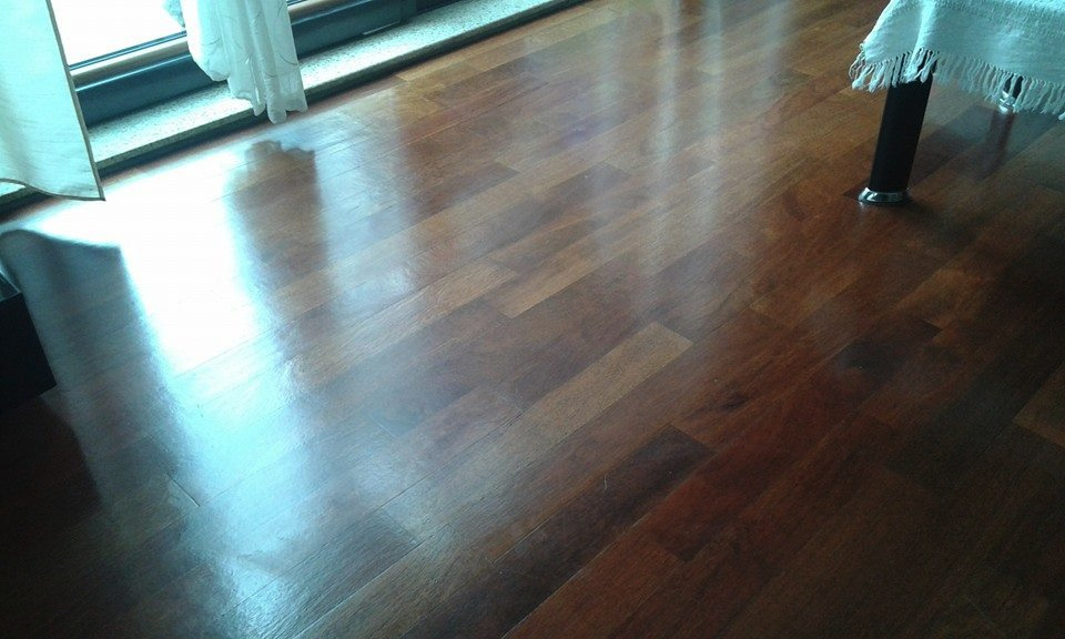 Błyszcząca, ciemnobrązowa podłoga z desek parkietowych, odbijająca światło z okna, widoczny fragment zasłony i nogi stołu z białym obrusem.