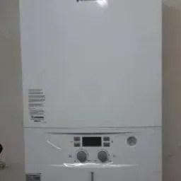 Biały, wiszący piec gazowy marki Junkers zamontowany na beżowej ścianie. Widoczne pokrętła regulacyjne i wyświetlacz cyfrowy.