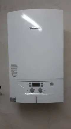 Biały, wiszący piec gazowy marki Junkers zamontowany na beżowej ścianie. Widoczne pokrętła regulacyjne i wyświetlacz cyfrowy.