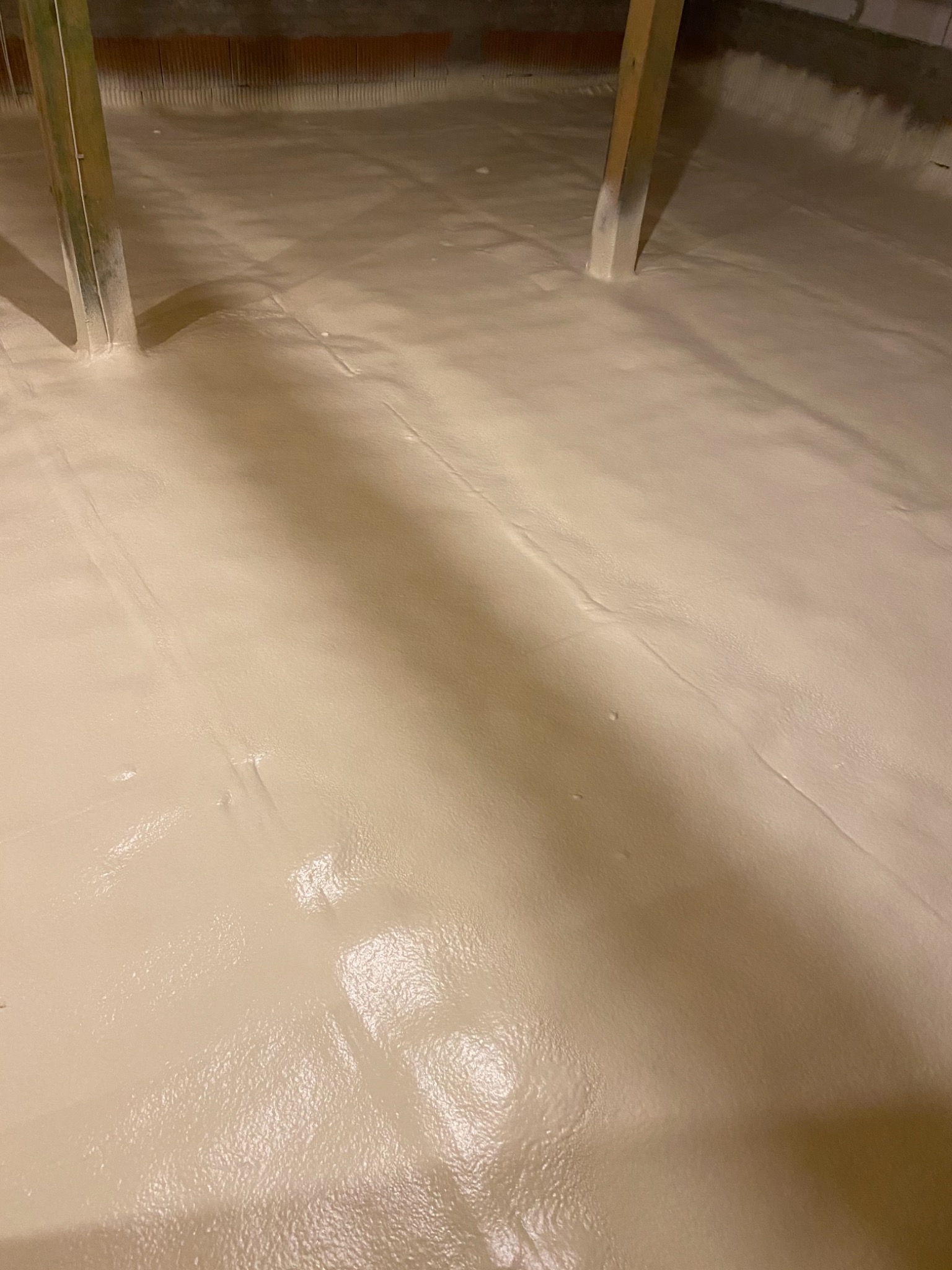 Poddasze po aplikacji jasnej pianki izolacyjnej, widoczne drewniane belki konstrukcyjne i nierówna powierzchnia izolacji.