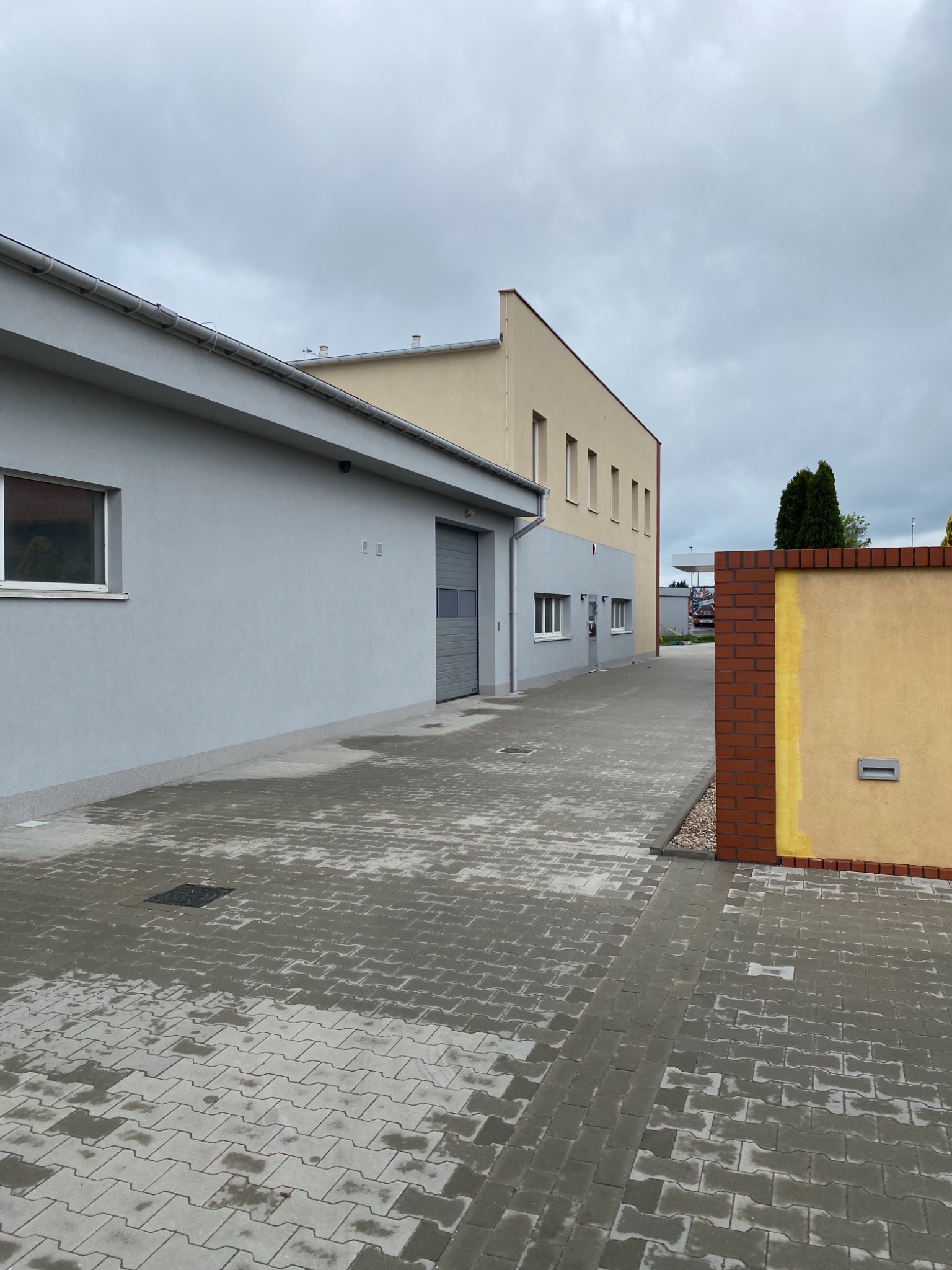 Szary budynek po remoncie z nową elewacją w Lesznie, widok z zewnątrz na wilgotny chodnik z kostki brukowej i fragment muru z żółtą ścianą.