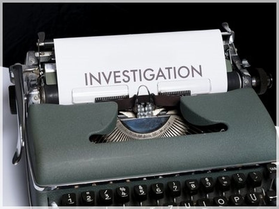 Stara maszyna do pisania z napisem 'INVESTIGATION' na kartce papieru, czarne tło.