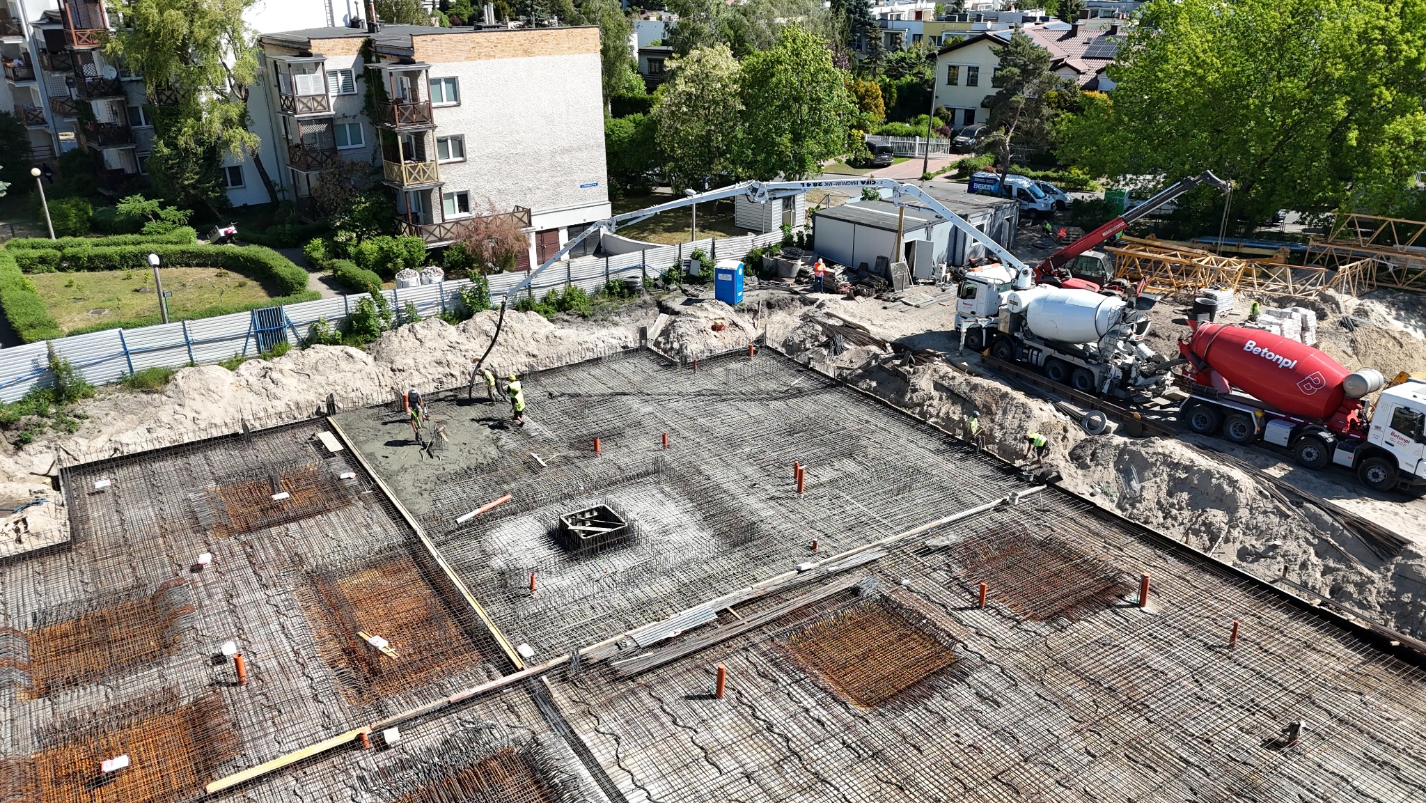 Zalewanie betonem zbrojonej płyty fundamentowej na budowie, widok z góry, w tle betonowozy i pompa do betonu.