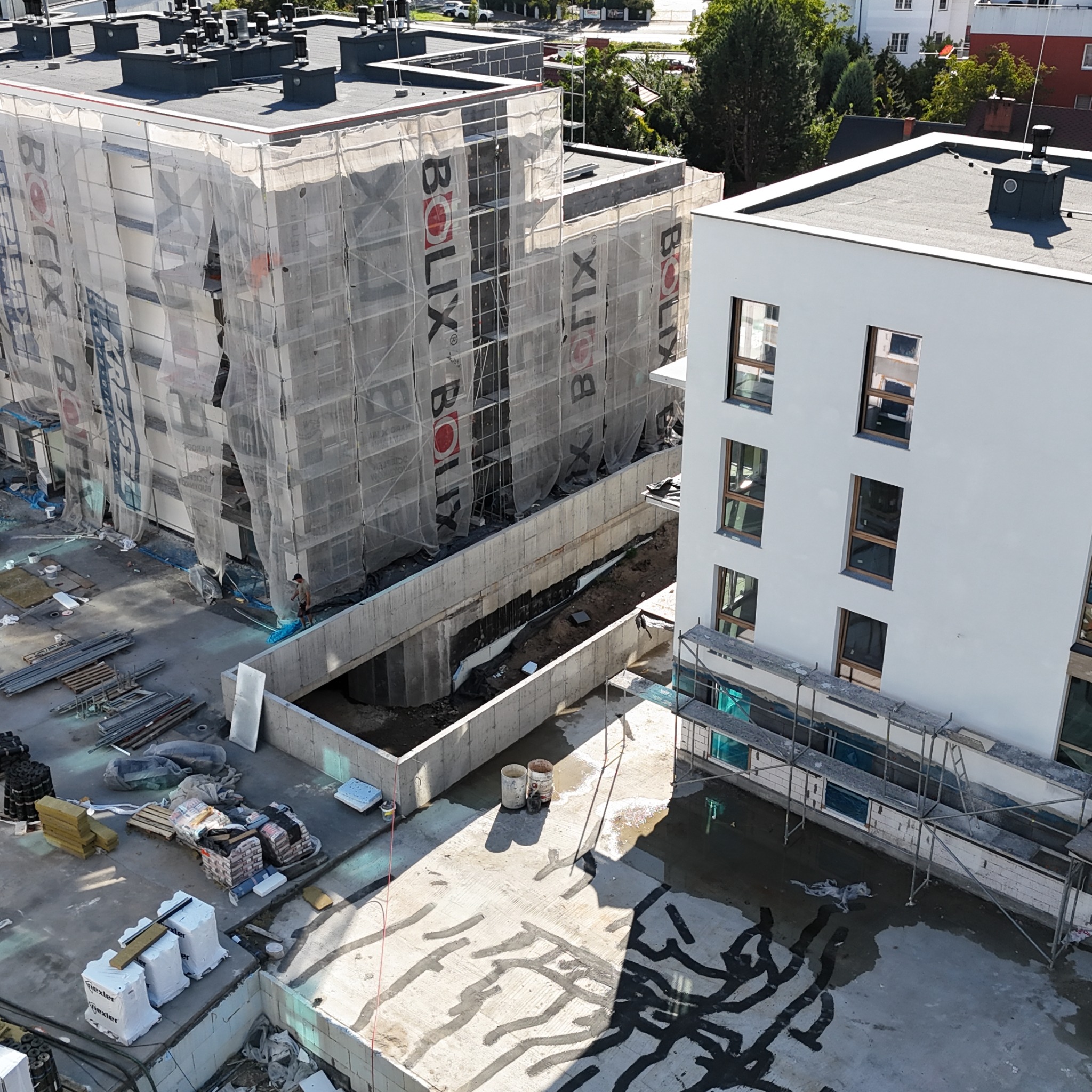 Budowa nowego budynku wielorodzinnego z rusztowaniami i siatkami ochronnymi. Widoczne materiały budowlane i elementy konstrukcyjne. Ujęcie z góry.