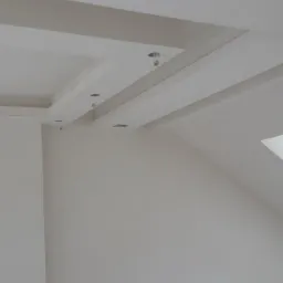 Białe, świeżo pomalowane ściany i sufit z dekoracyjnymi listwami, widoczne przygotowane otwory na oświetlenie punktowe.