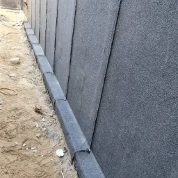 Fragment dachu pokrytego papą termozgrzewalną z widocznym betonowym obrzeżem i piaszczystym podłożem u podstawy.