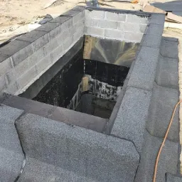 Wykończenie attyki dachowej z bloczków betonowych i papy bitumicznej, widoczne narzędzia i materiały budowlane na dachu.