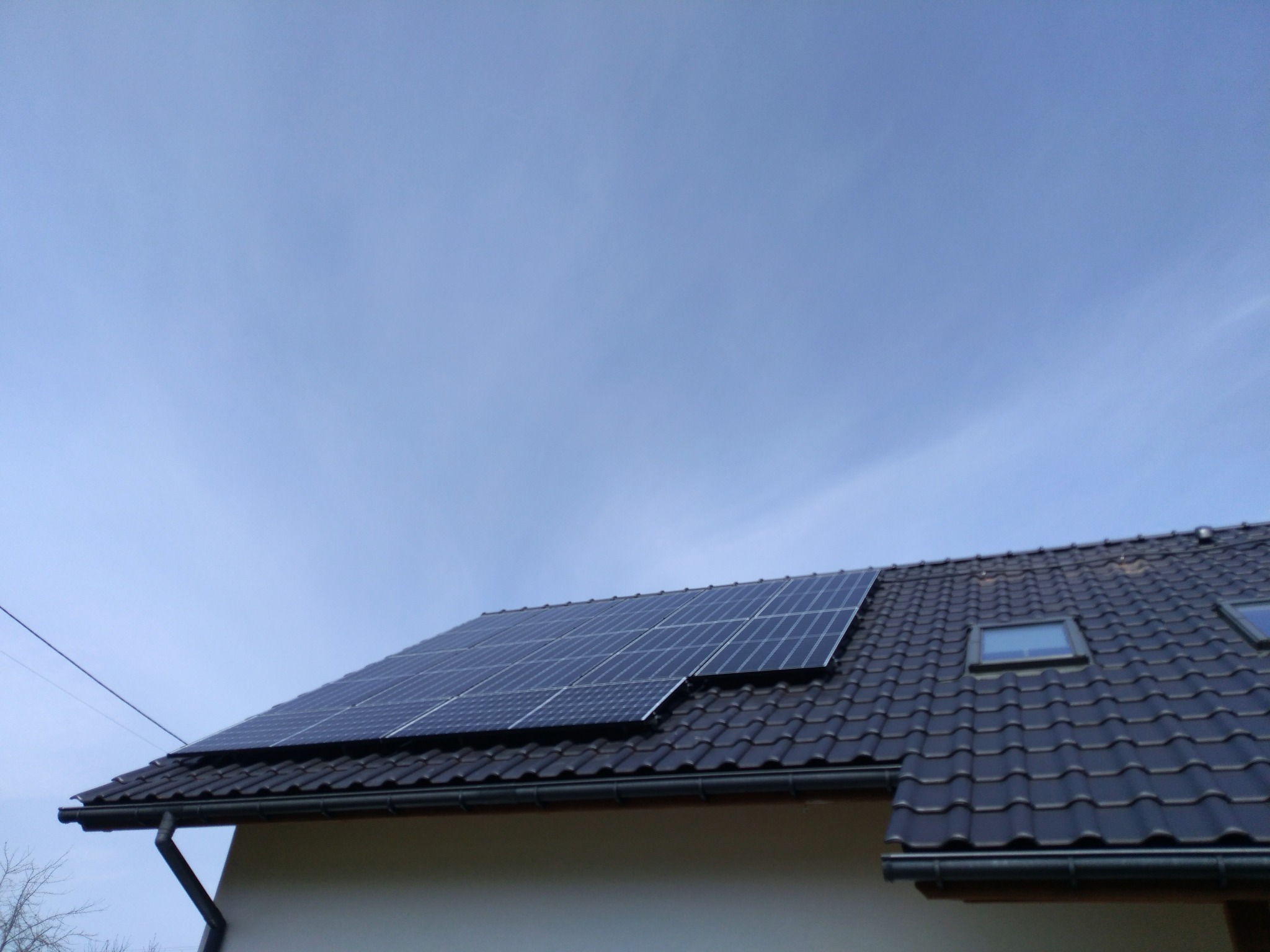 Panele słoneczne zamontowane na ciemnym dachu domu w Bielsku-Białej, widoczne okna dachowe i błękitne niebo.