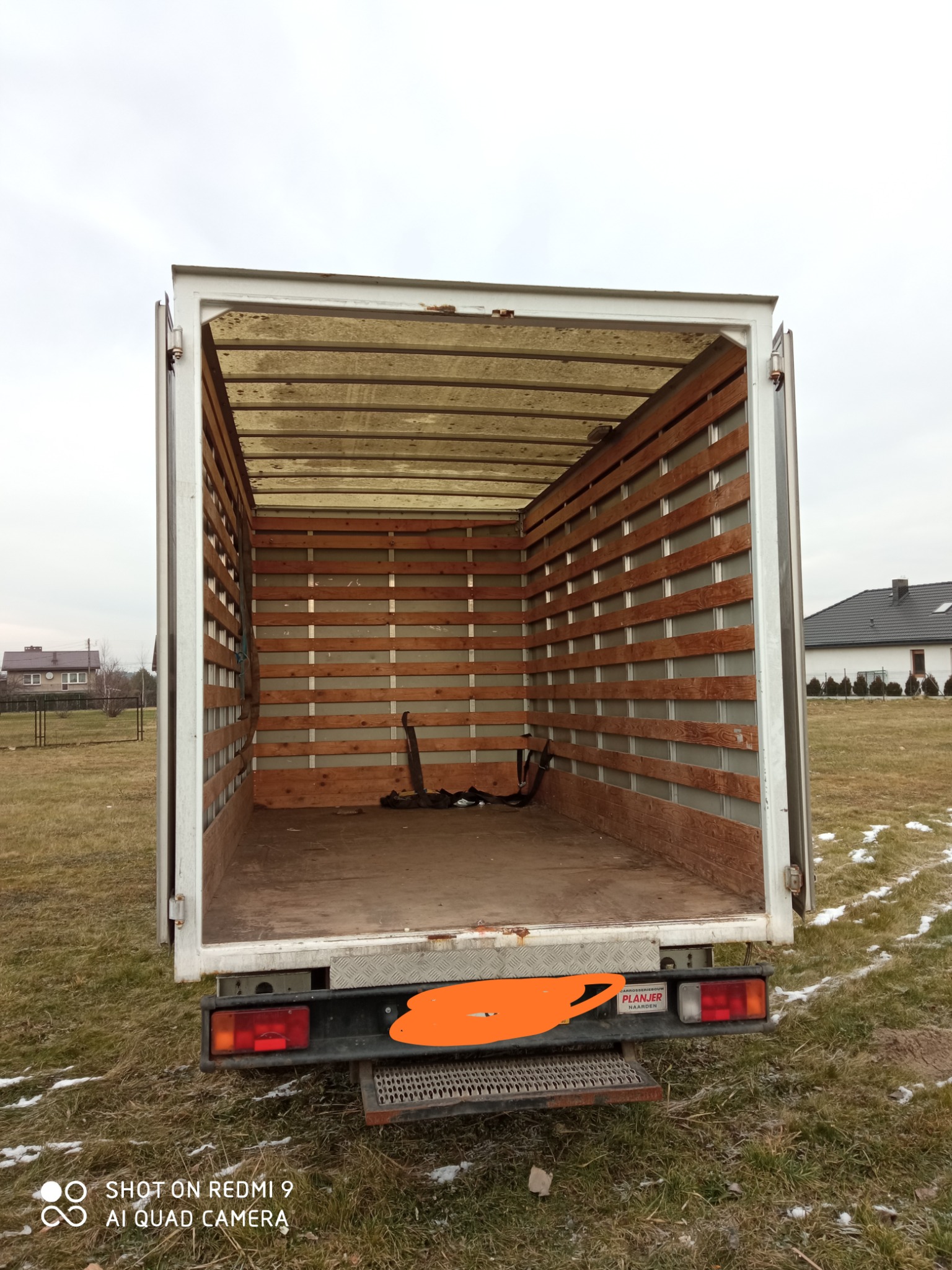 Pusta przestrzeń ładunkowa otwartego samochodu dostawczego z drewnianymi listwami, widok od tyłu, częściowo zamazana tablica rejestracyjna.