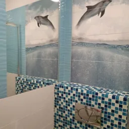 Wykończona łazienka z mozaiką w odcieniach błękitu i motywem delfinów na płytkach ściennych, widoczne elementy armatury i lustro.