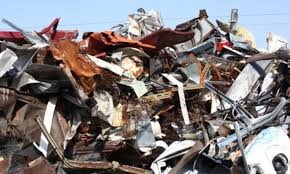 Stos pogniecionych, zardzewiałych blach i metalowych odpadów, widoczny w słoneczny dzień na zewnątrz.