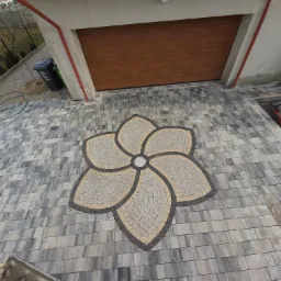 Ułożona kostka brukowa przed garażem z dekoracyjnym motywem kwiatowym z kostki w odcieniach szarości i beżu, widok z góry.