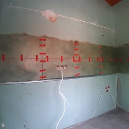 Jacek Morawski Usługi Remontowo-Budowlane ALANIS - Przygotowanie ściany z płyty karton gips do układania płytek, widoczne profile metalowe, wyprowadzone przewody elektryczne i czerwone krzyżyki do poziomowania płytek.