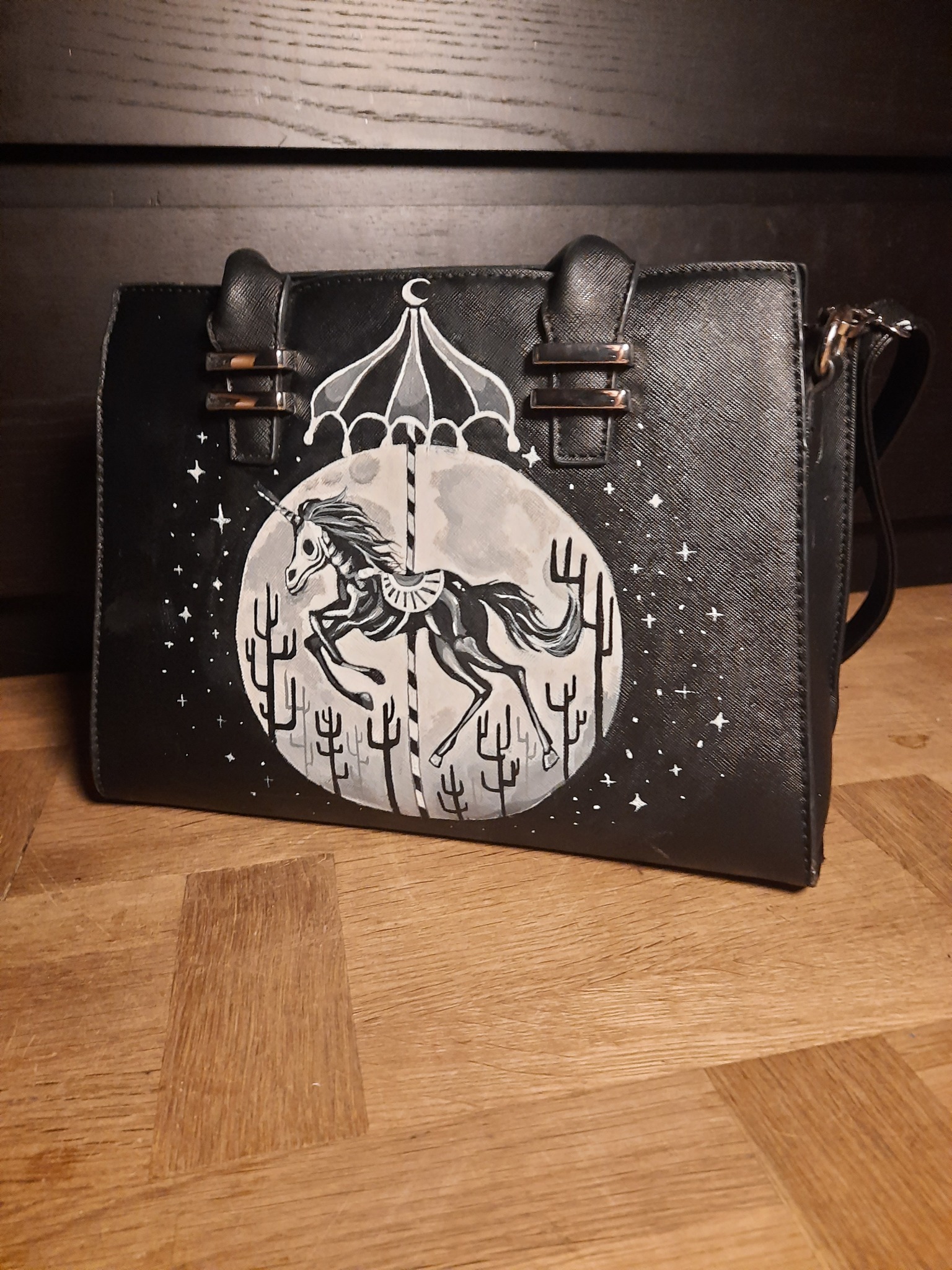 Czarna torebka z ręcznie malowanym motywem karuzeli z szkieletem jednorożca na tle księżyca i kaktusów.