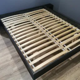 Drewniana rama łóżka z listwami w Bielsku-Białej, widok z góry na podłodze imitującej drewno, szare ściany w tle.