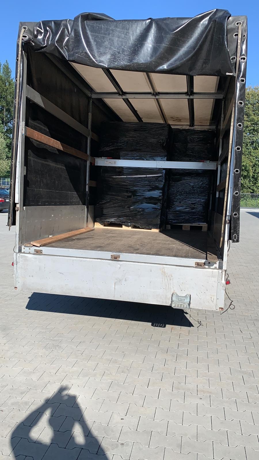 Wnętrze paki samochodu dostawczego z czarną plandeką, załadowane paletami z towarem owiniętym czarną folią stretch.