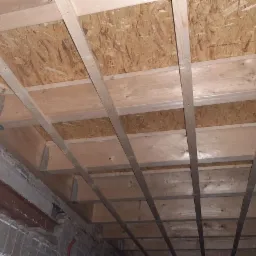 Konstrukcja drewniana poddasza z płytą OSB, widoczne metalowe łączniki i belki nośne, surowy stan przed ociepleniem.