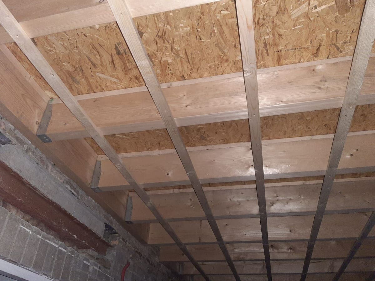 Konstrukcja drewniana poddasza z płytą OSB, widoczne metalowe łączniki i belki nośne, surowy stan przed ociepleniem.