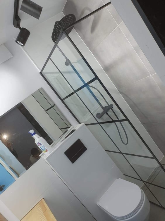 Nowoczesna kabina prysznicowa z czarną ramą i deszczownicą, widok z dołu, obok toaleta i butelka środka czyszczącego na zabudowie.