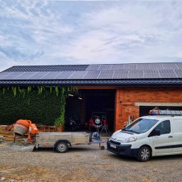 NORTMAR Sp. z o. o. - Ceglany budynek z panelami słonecznymi na dachu, obrośnięty bluszczem, z zaparkowanym białym vanem z drabiną na dachu, przyczepką z gruzem, betoniarką i stertą desek na żwirowym podłożu.