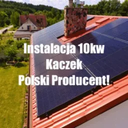 Panele fotowoltaiczne 10kW na czerwonym dachu domu jednorodzinnego, widok z góry, zielony trawnik i drzewa w tle.