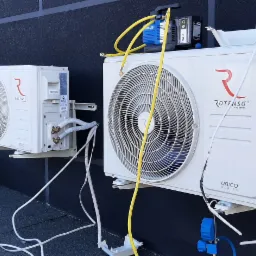 Dwa klimatyzatory marki Rotenso zamontowane na zewnątrz budynku w Ostrowie Wielkopolskim, podłączone do przewod&oacute;w i pompy pr&oacute;żniowej podczas serwisu.