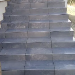 Zewnętrzne schody wejściowe wyłożone szarymi płytkami ceramicznymi, widoczne niedociągnięcia w fugowaniu przy ścianie budynku.