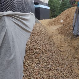 Michał Makowski - Ocieplenie fundamentów budynku z użyciem folii kubełkowej i geowłókniny, obsypane drobnym żwirem. Widoczny fragment pracownika z łopatą.