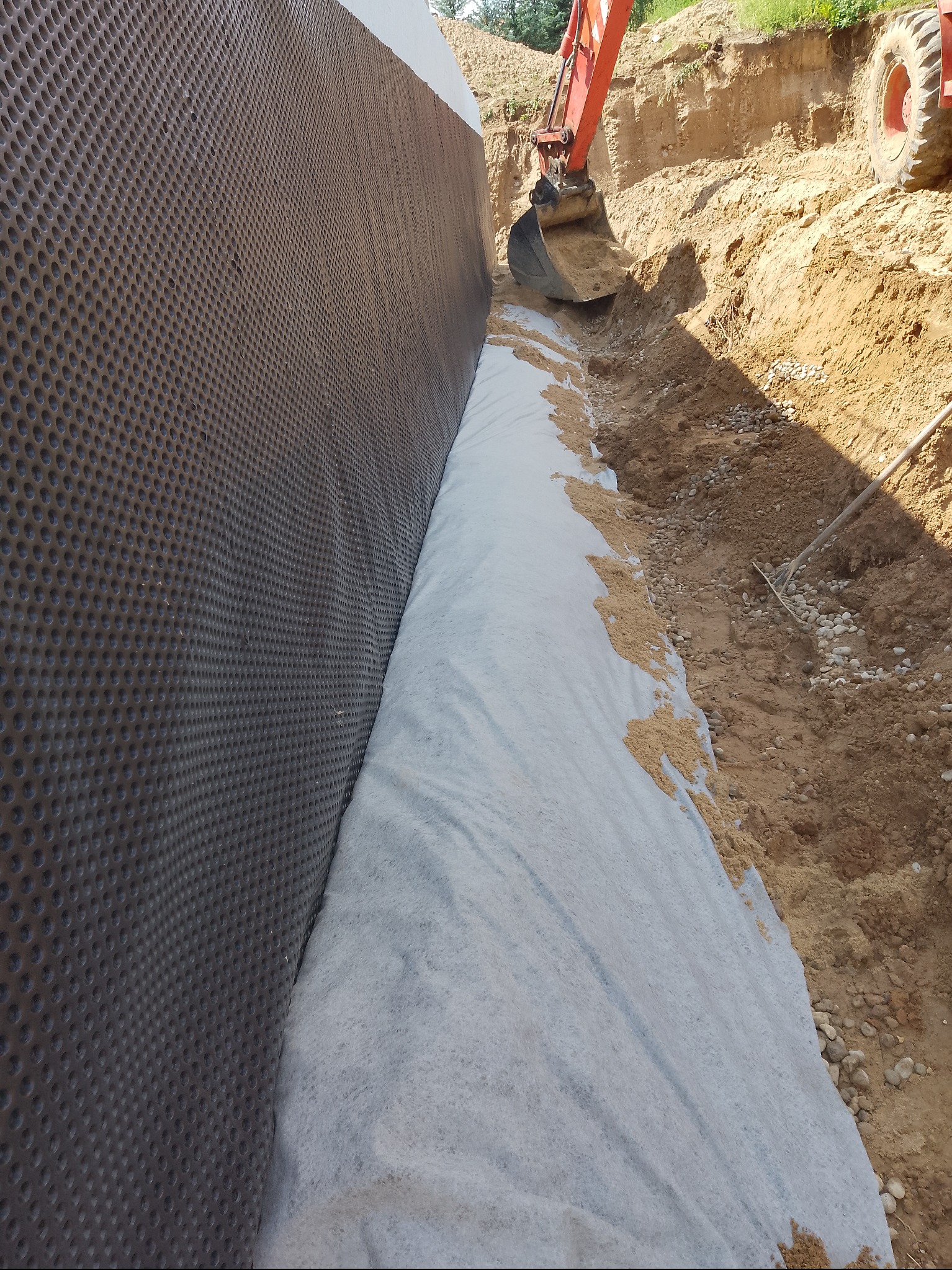 Ochrona fundamentów: folia kubełkowa, geowłóknina i wykop z koparką. Etap prac ziemnych przy izolacji pionowej fundamentów.