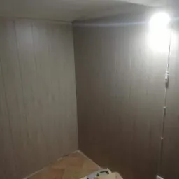 Wnętrze wykończone panelami ściennymi w odcieniach beżu i brązu, widoczna instalacja elektryczna z włącznikiem na ścianie, fragment podłogi z brązowych płytek.