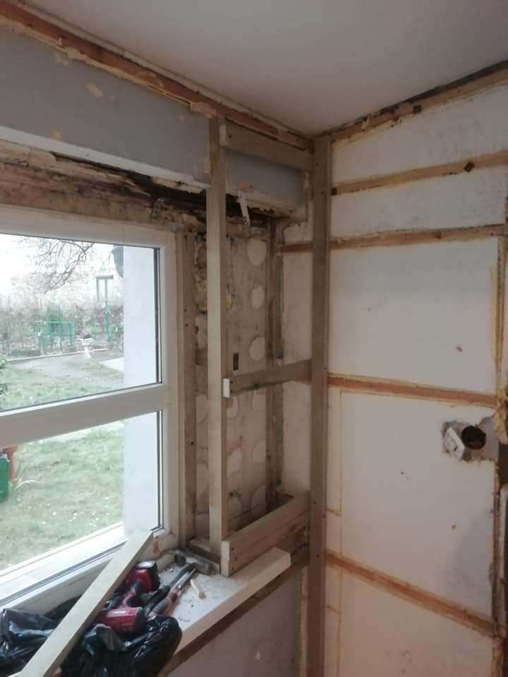 Demontaż starej ściany w pomieszczeniu z oknem, odsłonięta konstrukcja drewniana, widoczne narzędzia na parapecie, przygotowanie do dalszych prac remontowych.