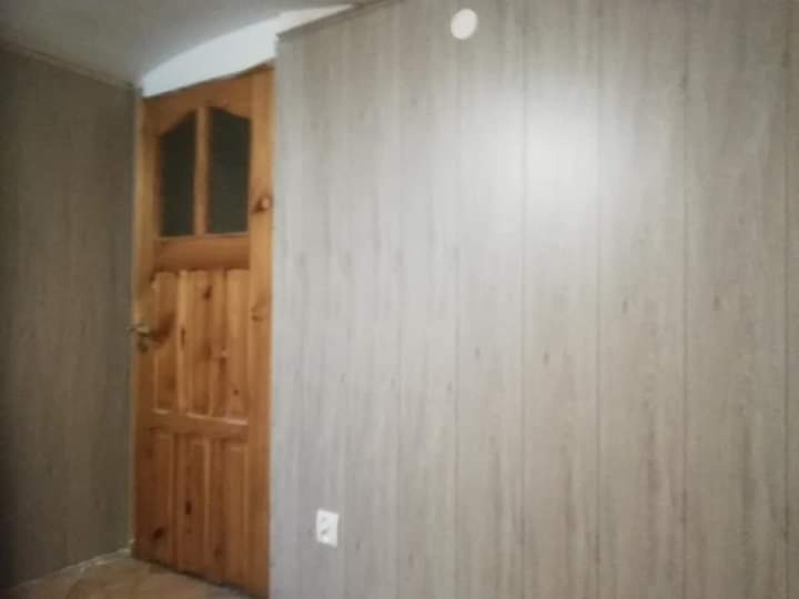 Wnętrze po remoncie: drewniane drzwi z szybkami, ściany wyłożone panelami imitującymi drewno, widoczny fragment podłogi i gniazdko elektryczne.