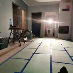 Artur Rodak Remonty i wykonczenia - Przygotowanie podłoża pod panele w mieszkaniu w Głogowie: rozłożona pianka podkładowa z wyznaczonymi liniami cięcia, widoczna piła stołowa i narzędzia.