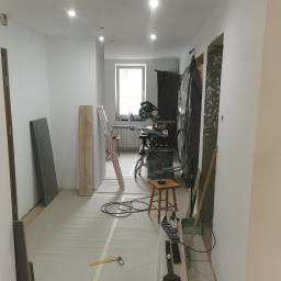 Artur Rodak Remonty i wykonczenia - Wnętrze w trakcie prac wykończeniowych: widoczne przygotowane panele podłogowe Swiss Krono, narzędzia, folia ochronna na podłodze i ściany przygotowane do malowania.