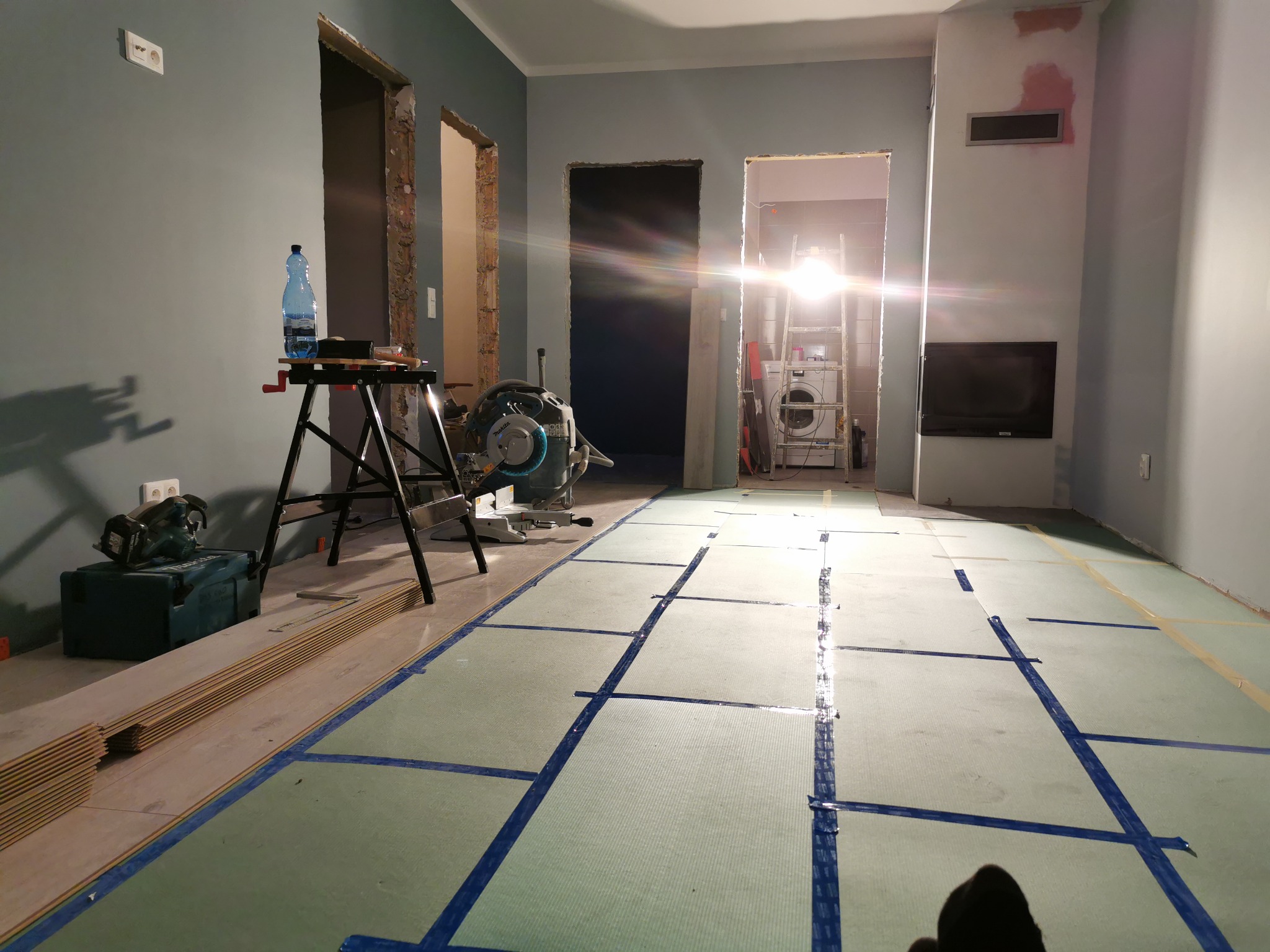 Przygotowanie podłoża pod panele w mieszkaniu w Głogowie: rozłożona pianka podkładowa z wyznaczonymi liniami cięcia, widoczna piła stołowa i narzędzia.