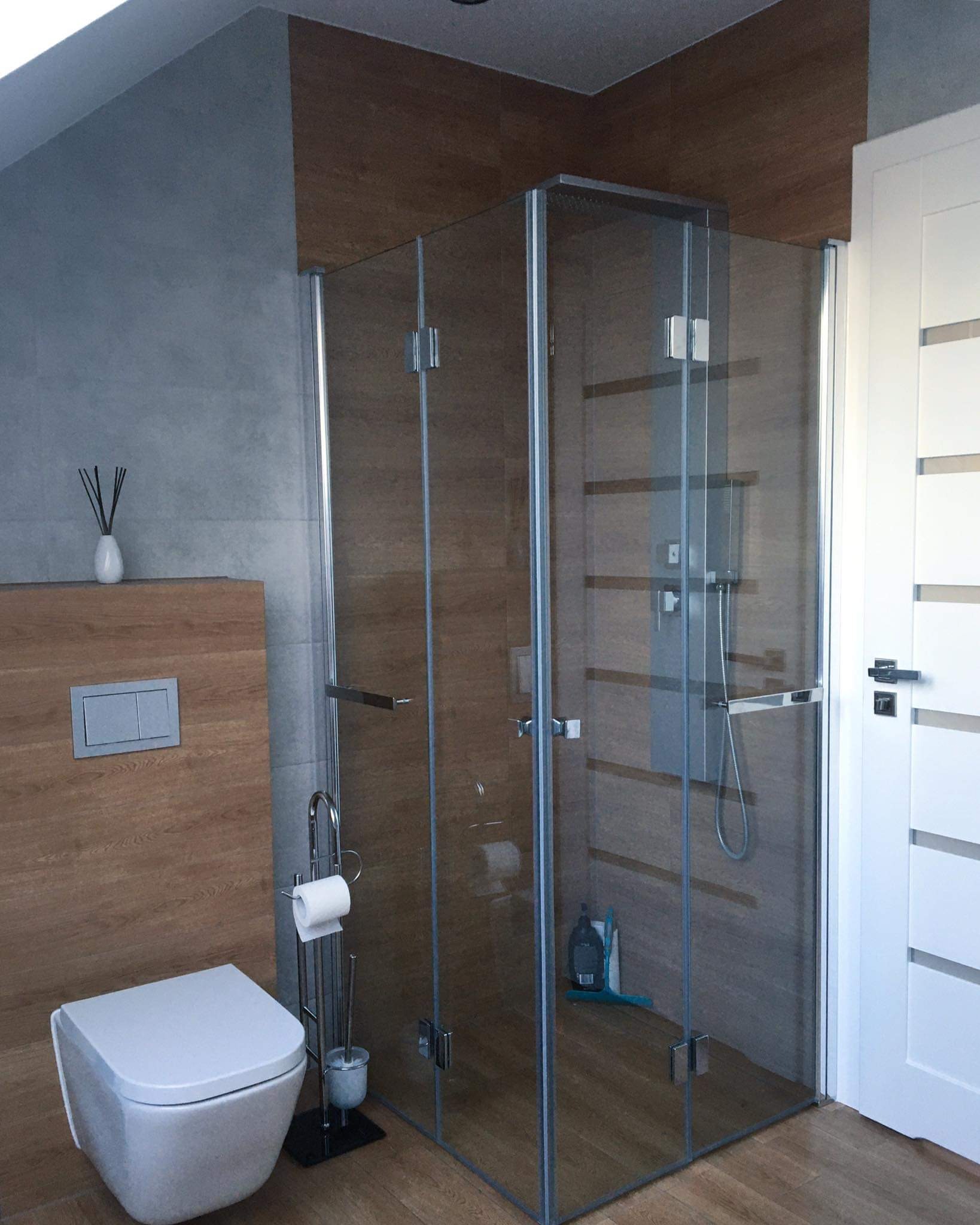Nowoczesna łazienka z kabiną prysznicową ze szkła hartowanego, wiszącą toaletą i drewnopodobnymi płytkami na ścianach i podłodze.