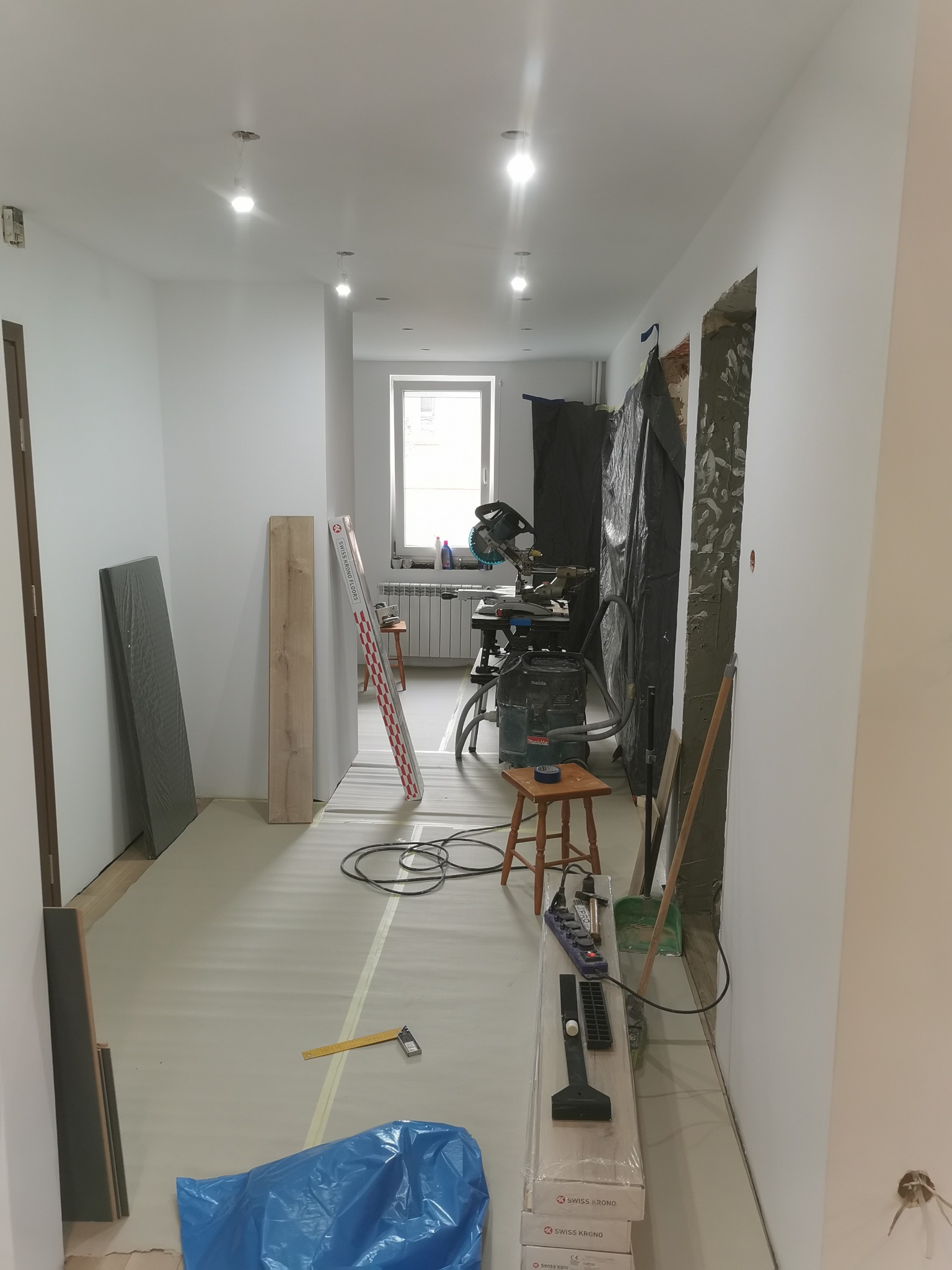 Wnętrze w trakcie prac wykończeniowych: widoczne przygotowane panele podłogowe Swiss Krono, narzędzia, folia ochronna na podłodze i ściany przygotowane do malowania.