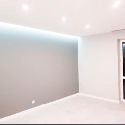 Express Remont - Świeżo pomalowane wnętrze z szarą ścianą z listwą LED pod sufitem i białymi ścianami, widoczny kontakt elektryczny przy podłodze.