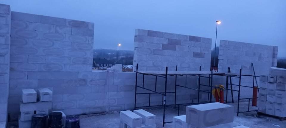 Wznoszenie ścian domu z bloczków betonu komórkowego Ytong, widoczne rusztowanie i zapas bloczków, pochmurne niebo w tle.