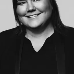 Portret uśmiechniętej kobiety w czarnej marynarce na jasnym tle, zdjęcie czarno-białe.